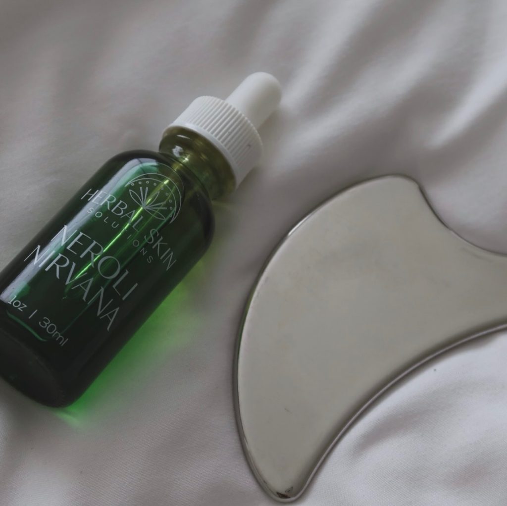 bottle of natural skin care solution and gua sha tool for facials